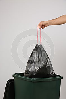 Man throwing garbage bag into bin on light background, closeup