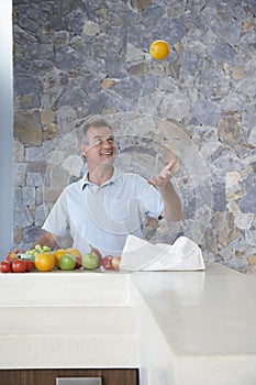 Man Throwing Orange Into Air At Kitchen Counter