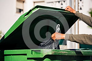 Man throwing out black eco-friendly recyclable trash bag in to big plastic green garbage container. Take out the trash