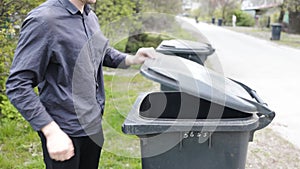 Man throwing out black eco-friendly recyclable trash bag in to big plastic green garbage container. Take out the trash