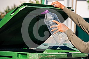 Man throwing out empty non-recyclable plastic aqua bottle in to green garbage container