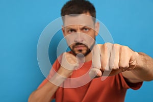Man throwing punch against light blue background, focus on fist. Space for text