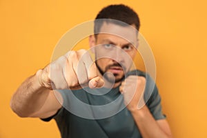 Man throwing punch against orange background, focus on fist. Space for text