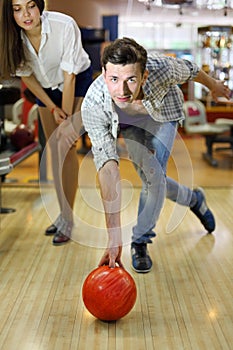 Man throws ball in bowling; woman looks at man