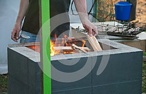 A man throws dry branches into the grill fire. Preparing fire for barbeque meat