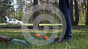 A man throws garbage in the forest, in the background a car