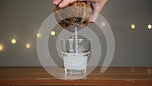 Man throws ice into a glass, then pours coconut water. Against the background of the lights