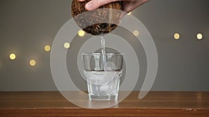 Man throws ice into a glass, then pours coconut water. Against the background of the lights