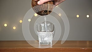 Man throws ice into a glass, then pours coconut water. Against the background of the lights