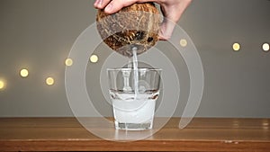 Man throws ice into a glass, then pours coconut water. Against the background of the lights