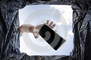 Man throws a non-working smartphone into a trash can. Bottom view from the trash can. The problem of recycling and pollution of
