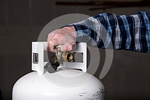 Man tightens the knob on a white propane tank with his hand