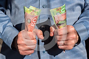 Man tightly holding Canadian twenty and fifty dollar bills in both hands