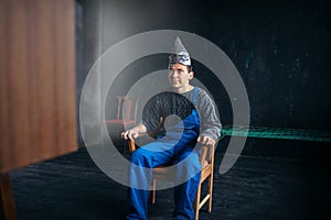 Man in tinfoil hat sits in chair, paranoia concept