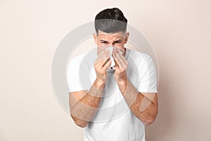 Man with tissue suffering from runny nose on beige background