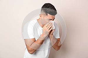 Man with tissue suffering from runny nose on beige background