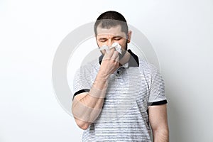 Man with tissue suffering from runny nose on white background