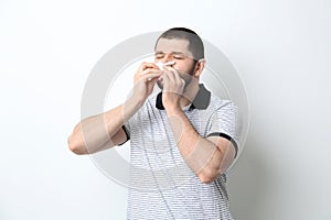 Man with tissue suffering from runny nose on white background