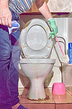A man with a toilet brush cleans an old dirty toilet bowl