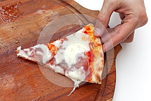 Man took last one slice of delicious Italian pizza. In frame hand taking slice of hot pizza with ham on wooden board