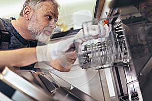 Man with toolbox repairing dishwasher in a household