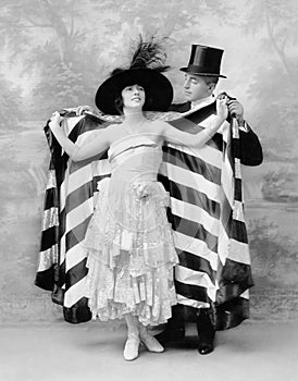 Man in a top hat helping a woman into a cape