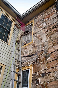 Man on top of a ladder against an old stone home does roof repairs