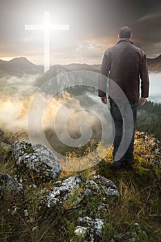 Man on top of the mountain looking at the Christian Cross