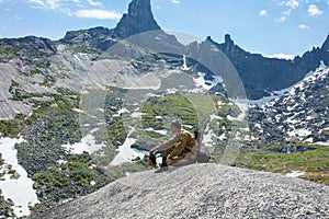 The man at top of the rock satisfies thirst and enjoys a beautiful landscape.