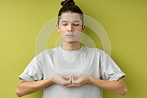 man with topknot stand meditating, keeping calm, isolated over green studio background