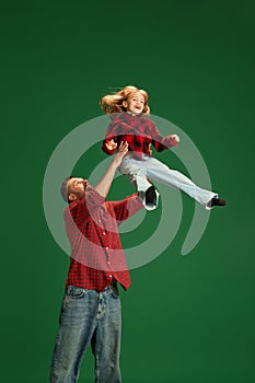 Man tosses into air his playful and partying daughter, little girl against green studio background. Concept of