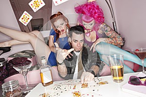 Man tossing playing cards in air with women sitting besides him