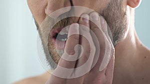 Man touching cheek feeling toothpain in bathroom, caries, pulp inflammation