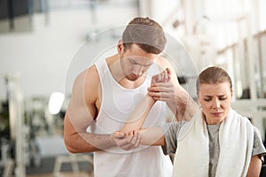 Man touching female painful elbow at gym.