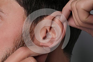 Man touching his ear on grey background, closeup