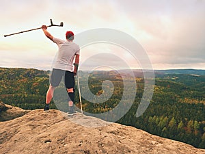 Man tourist after accident use knee brace features and forearm crutches. Man looking over