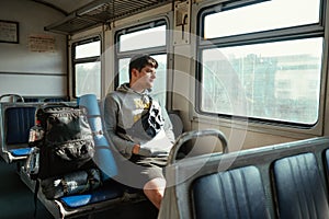 Man tourist with a backpack rides a train in the mountains and looks out the window