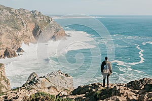 A man tourist with a backpack stands in solitude at Cape Roca in Portugal