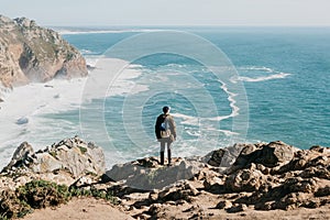 A man tourist with a backpack stands in solitude at Cape Roca in Portugal
