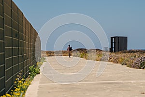Man tourist with backpack walk along walking path at rocky coast of Mediterranean Sea in city Paphos of Cyprus in summer