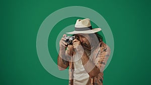 Man tourist in casual clothing and straw hat taking photos on old film camera. Isolated on green background.