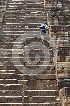 Man tourist climbs the high stair of ancient temple. Endless steps of ancient buddhist temple in Angkor Wat.