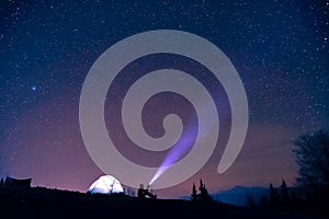 Tourist with flashlight near his camp tent under a sky full of stars, night mountain loneliness