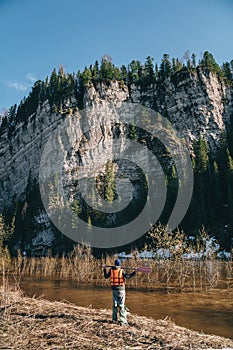 Man tourist holding puddle standing near high stone wall, back view. Rafting on mountain river at spring season.