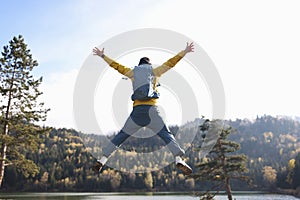 Man tourist with open arms jumping, lake and mountains on background