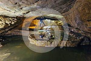 Man tourist speleologist in wetsuit with flashlight in beautiful natural cave