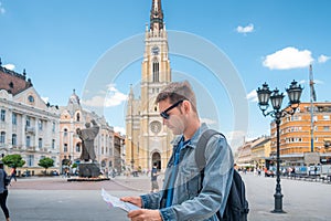 Man tourist on the square in the city with sightseeing map looking for landmarks. Handsome male traveler backpacker in