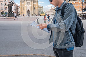 Man tourist on the square in the town with paper map looking is exploring new city. Handsome male traveler backpacker in