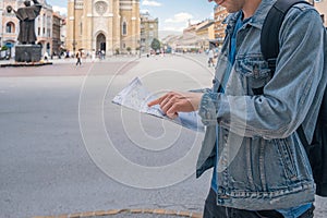 Man tourist on the square in the town with paper map looking for hotel he booked. Male traveler backpacker holding map