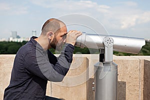 Man tourist standing on building rooftop looking through binocular telescope
